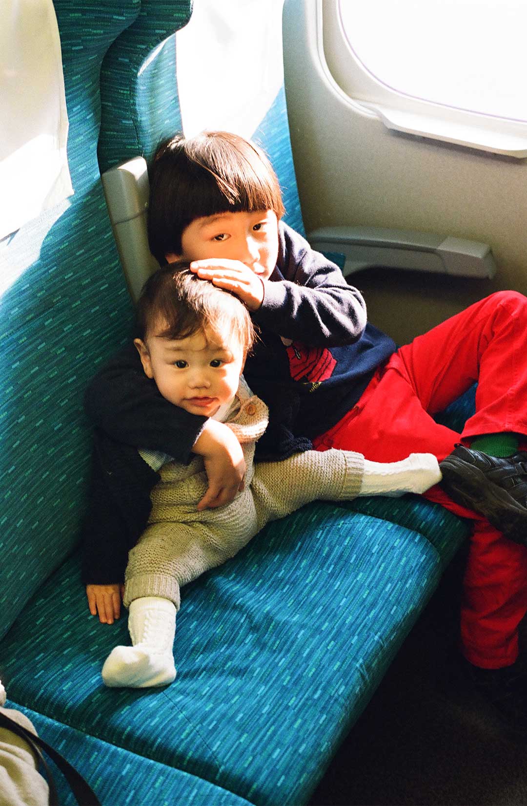 電車の席に兄弟で座っている。お兄ちゃんは赤ちゃんの頭を撫でている。