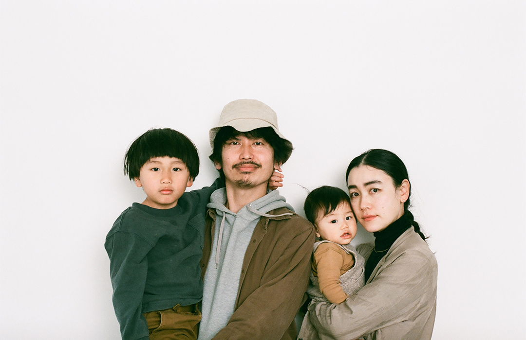 白い背景の前で家族4人で写真を撮る。パパはお兄ちゃんをママは赤ちゃんを抱っこしている。