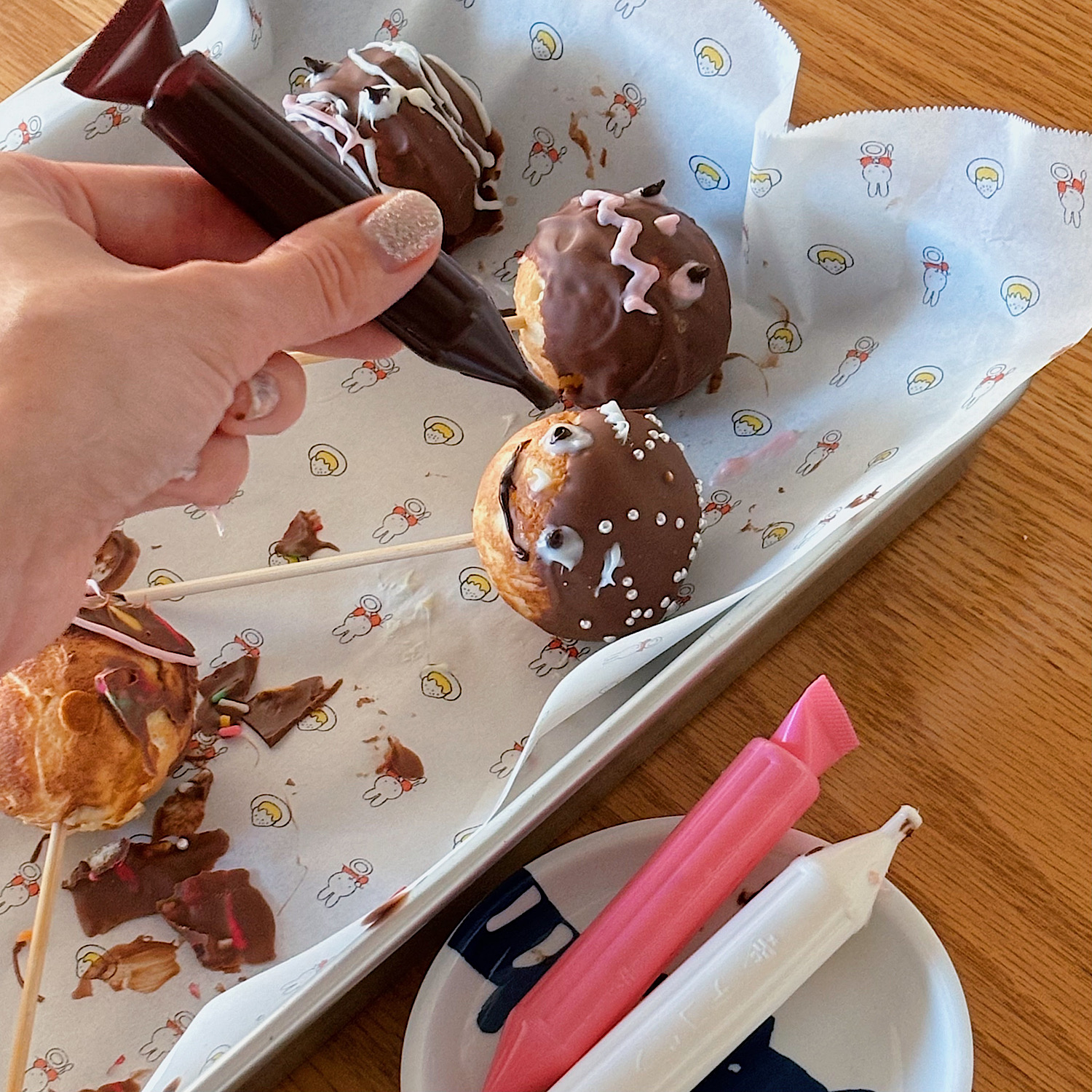 ハロウィンパーティにも最適♪たこ焼き器でつくる簡単＆楽しい＜ホットケーキポップス＞。コーティングしたチョコが固まるまで冷蔵庫で冷やしたら、デコペンで顔を描いていく。